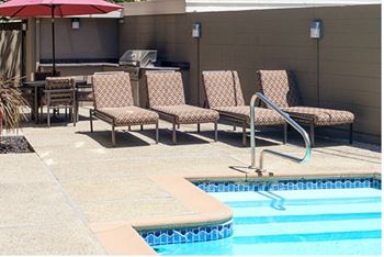 A pool with a red umbrella and chairs around it.